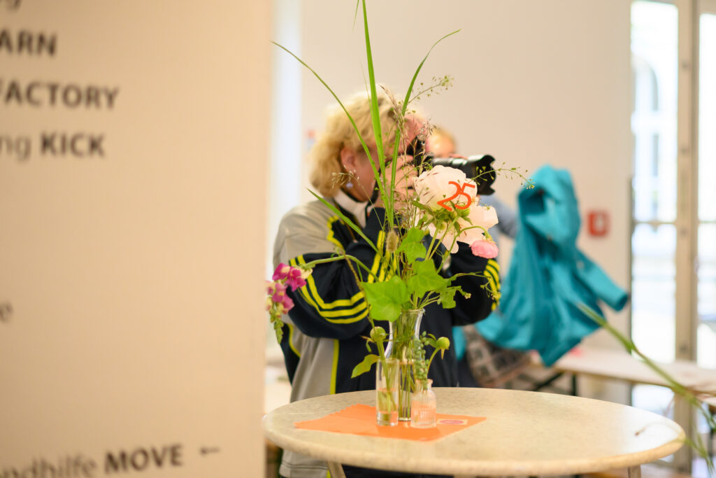 A person with the camera is taking photos. And in front is a table with flowers.
