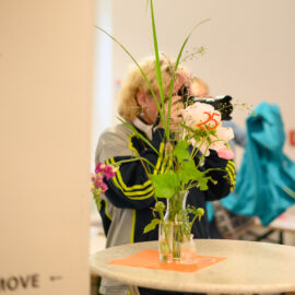 A person with the camera is taking photos. And in front is a table with flowers.